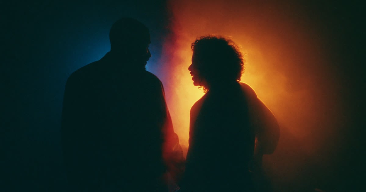 A man and a woman flirting, seen in silhouette against blue and amber light